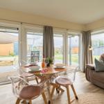 Essbereich mit Tisch und transparenten Stühlen. Sofa mit Kissen. Blick auf Terrasse und Garten.