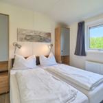 Zwei Einzelbetten mit weißen Bettwäschen, Wandspiegel und Fenster mit Blick auf Grün.