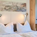 Zwei Betten mit weißen Kissen und Bettwäsche unter einer Wanddekoration mit zwei Wandlampen.