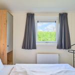 Schlafzimmer mit Bett, Fenster und Gardinen.