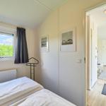 Schlafzimmer mit Fenster, Bett und Blick auf Grünflächen. Durchgang zur Küche.