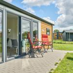 Terrasse mit Tisch, zwei roten Stühlen und Grill. Glasfront öffnet sich zum Innenraum.