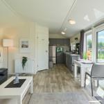 Wohnbereich mit Küche, Esstisch und Schlafzimmer. Holzboden, große Fenster und Balkon.