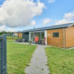 Moderne Holzhütte mit Terrasse, Garten und Grillplatz unter blauem Himmel.