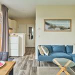 Wohn- und Essbereich mit blauem Sofa, Glas-Tisch und Küchenbereich im Hintergrund.