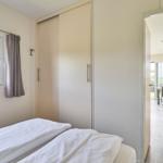 Schlafzimmer mit Doppelbett, Schrank und Fenster. Durchgang zur Küche.