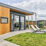 Moderne Holzhütte mit Terrasse und Liegen im Grünen.