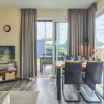 Wohn- und Essbereich mit TV, Tisch und Stühlen, großflächige Fenster zur Terrasse.