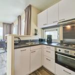 Küche mit weißen Schränken, Edelstahlherd und Blick auf Terrasse.