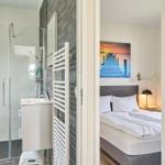 Schlafzimmer mit Bett und Wandbild. Nebenher Bad mit Dusche und Waschbecken.