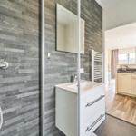 Badezimmer mit Dusche, Waschbecken und Toilette. Blick in die Küche.