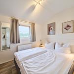 Schlafzimmer mit Doppelbett, Fenster, Spiegel und Wandbildern.