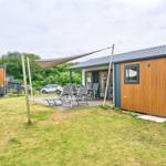 Haus mit Terrasse, Liegen und Sonnensegel. Grünfläche und Wald im Hintergrund.