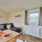 Wohnbereich mit Sofa, Esstisch und Fernseher. Fenster mit Vorhängen. Wandbilder und Uhr.