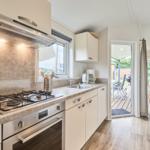 Küche mit Herd, Spüle und Fenster. Durchgang zur Terrasse und Essbereich.