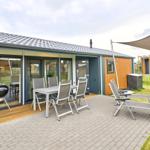 Terrasse mit Tisch, Stühlen, Liegestühlen und Grill. Sicht auf modernes Ferienhaus.