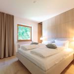 Schlafzimmer mit Doppelbett, Holzfußboden und Fenster mit Blick auf Bäume.