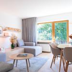 Wohn- und Essbereich mit Sofa, Tisch und Blick auf grüne Bäume.