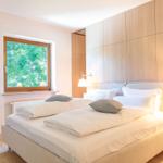 Schlafzimmer mit Doppelbett, Holzwand und Fenster mit Blick auf Bäume.