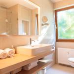 Badezimmer mit Waschbecken, Spiegel, Toilette und Fenster.