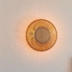 Wandlampe mit Holzrahmen und Strahlenmuster an der Wand.
