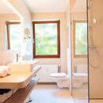 Badezimmer mit Dusche, Waschbecken und Toilette. Fenster mit Blick auf Grün.