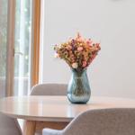 Ein runder Tisch mit Stühlen und einer Vase mit getrockneten Blumen.