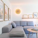 Ein Wohnzimmer mit grauem Sofa, Holztisch und Wandbildern.