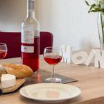 Tisch mit Wein, Brot und Käse, weiße Buchstaben und Blumen im Hintergrund.