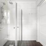 Dusche mit Glaswand, weißen Fliesen und dunklem Boden