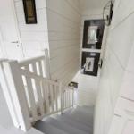 Helle Treppe mit weißem Geländer und Holzwänden. Wandbilder und Deckenleuchte sichtbar.