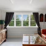 Wohnzimmer mit rotem Ledersofa, Glas-Tisch und Fensterblick auf Wald.