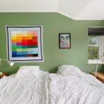 Schlafzimmer mit grünen Wänden, Doppelbett, Fenster und Kunst an der Wand.