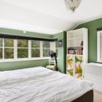 Schlafzimmer mit grünen Wänden, großem Fenster und weißem Bett.