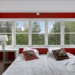 Schlafzimmer mit roten Wänden und großem Fensterblick auf Wald.