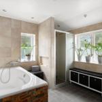 Badezimmer mit Badewanne, Dusche und Waschbecken. Fenster mit Pflanzen.