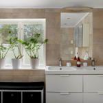 Badezimmer mit Waschtisch, Spiegel und Pflanzen am Fenster.