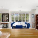 Esszimmer mit blauen Stühlen und großem Fenster. Holztisch im Vordergrund.