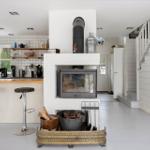 Küche mit Stehplatz, Kaminofen und Holzstapel. Hintergrund: Treppe und Fenster.