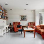 Wohnzimmer mit Klavier, Bücherregal und orangefarbenen Sitzmöbeln.