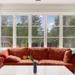 Ein Wohnzimmer mit rotem Sofa und großen Fenstern zum Garten.