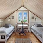 Zwei Betten, Tisch mit Stühlen, Fenster, Holzdecke und Boden.