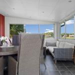Terrasse mit Sitzgruppe, Tisch und Stühlen. Große Fenster mit Blick auf Landschaft.