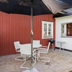 Terrasse mit Tisch, Stühlen, Sonnenschutz und Grill vor rotem und weißem Haus.