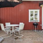 Terrasse mit Tisch, Stühlen, Sonnenschirm und Grill vor rotem Holzhaus