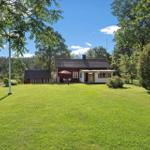 Roter Holzhaus mit Terrasse und Garten. Umgeben von Bäumen und Grasflächen.
