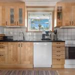 Küche mit Holzschränken, Waschmaschine und Fenster mit Blick.