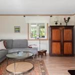 Wohnzimmer mit Sofa, Tisch und Holzschrank. Fenster, Kamin und Holzfußboden.