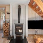 Wohnzimmer mit Kaminofen, Holzstapel und TV an der Wand.