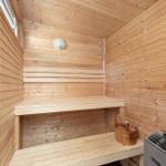 Sauna mit Holzbank, Holzwand und Holzdecke. Holzschale und Ofen sind vorhanden.